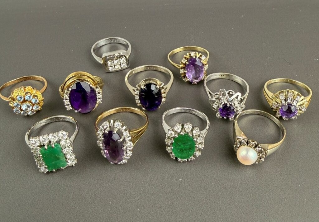 Elf Goldringe mit Amethysten, Smaragden, Brillanten und einer Perle auf grauem Grund